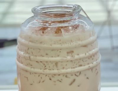 Un frasco de vidrio en forma de barril con una bebida cremosa color café claro y hielo