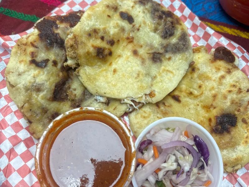 Pupusas en papel a cuadros con salsa roja y curtido