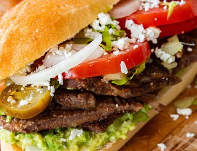 Una torta con carne a la plancha, aguacate, tomate, cebolla, jalapeño y queso blanco